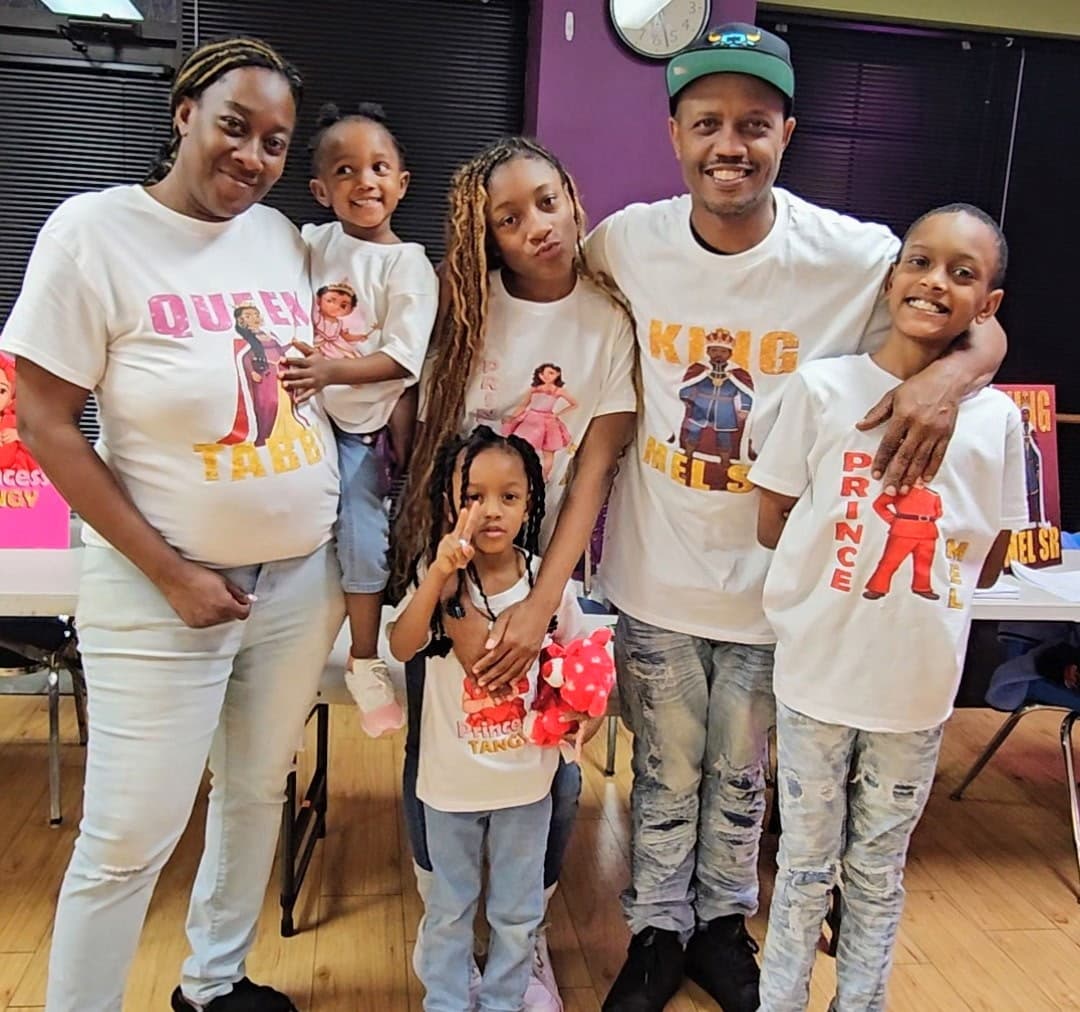 Smiling family of six wearing matching white t-shirts with royal-themed graphics and names.