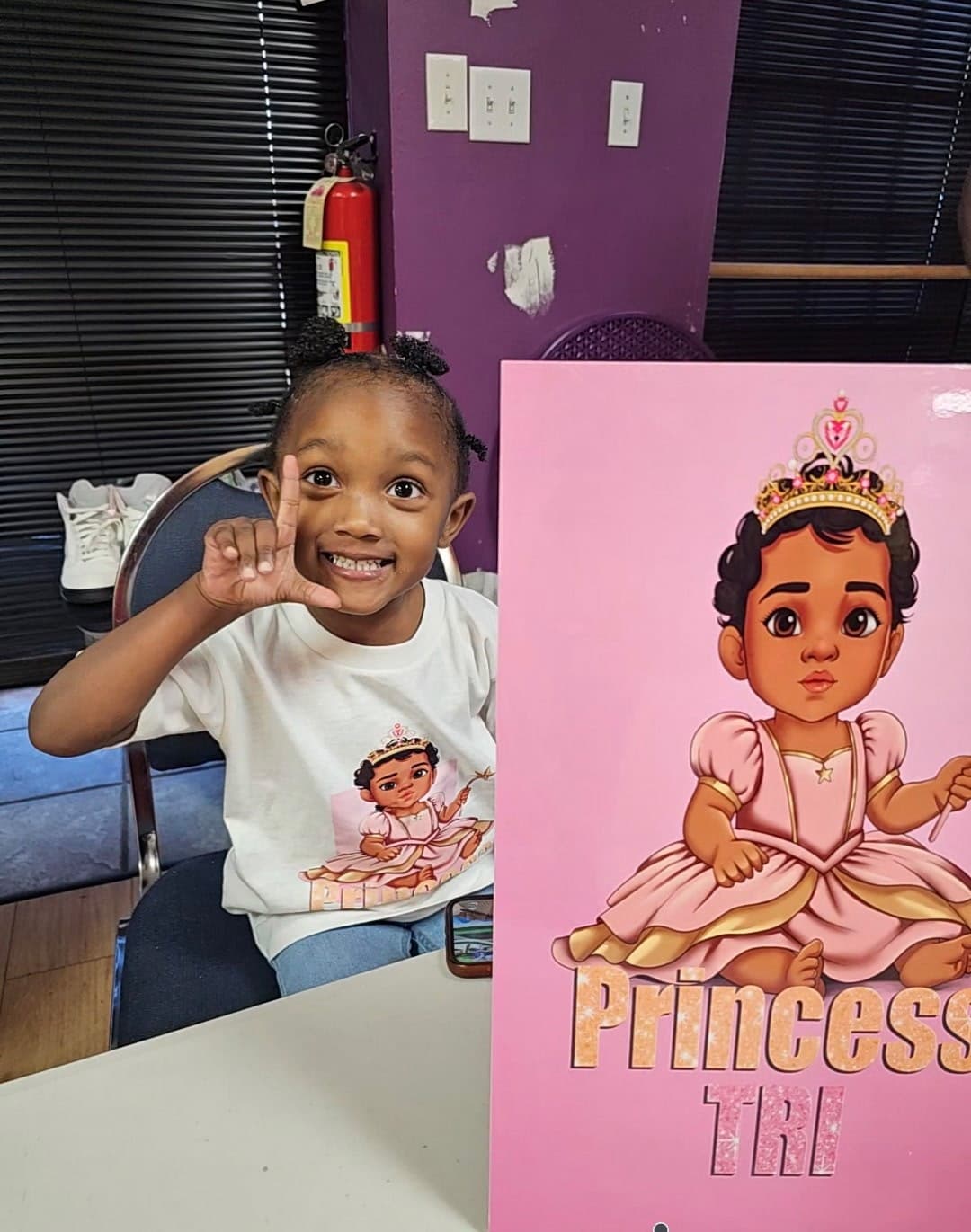 Smiling young girl in a princess shirt poses next to a matching pink princess poster.